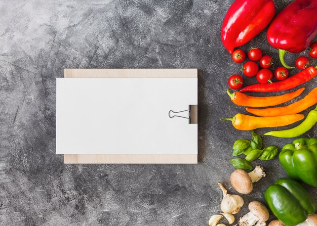 Colorful vegetables with blank paper on clipboard against grunge background