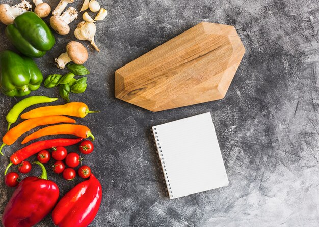 Free photo colorful vegetables on wooden board with spiral notebook and wooden board on concrete background