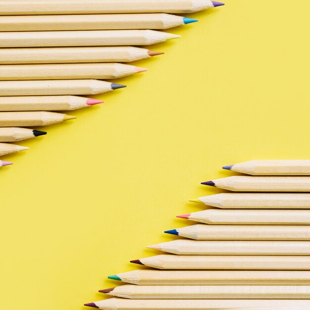 Colorful wooden pencils in a row on yellow backdrop