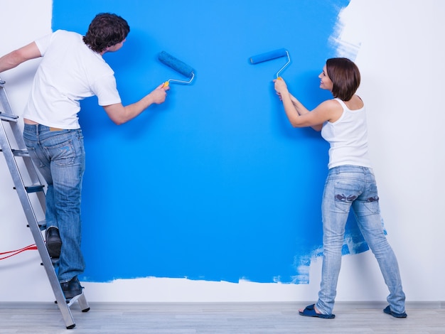 Free photo coloring the wall in blue by young couple in casuals