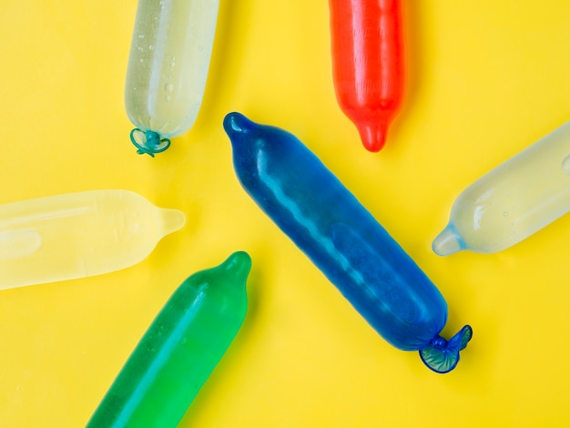 Colourful condoms filled with water on yellow background