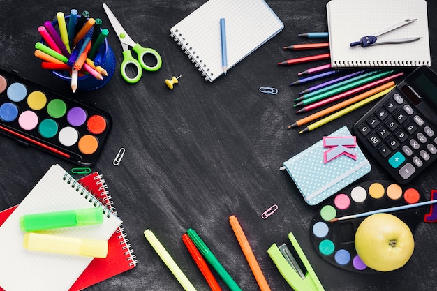 Colourful creative stationery, calculator and apple on dark background