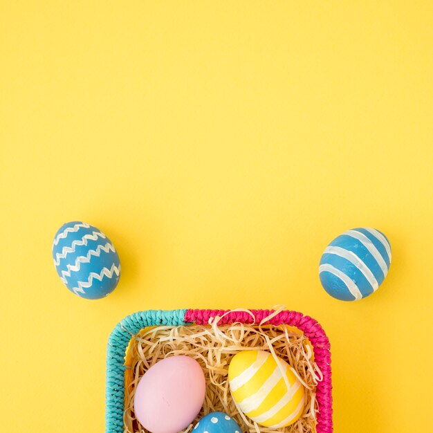 Colourful Easter eggs in  basket on yellow table 