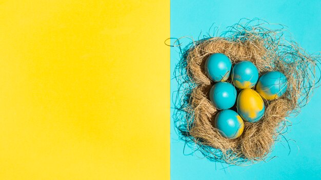 Красочные пасхальные яйца в большом гнезде на ярком столе