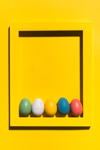 Foto gratuita uova di pasqua variopinte nel telaio sulla tavola gialla