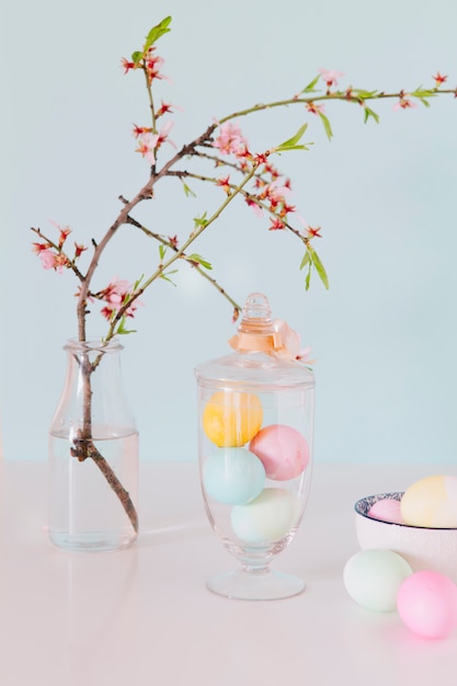 Colourful Easter eggs near flower twig in vase with water and bowl