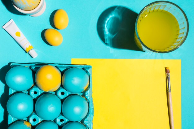 Colourful Easter eggs in rack with paint brush, glass of water and paper