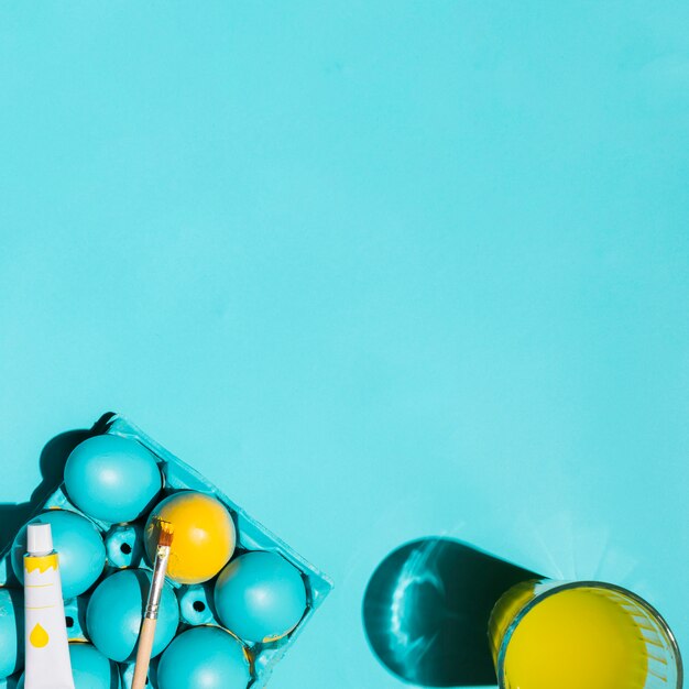 Colourful Easter eggs in rack with paint brush and glass of water on table