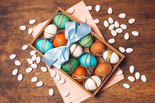 Colourful eggs in box on pink craft paper near little stones