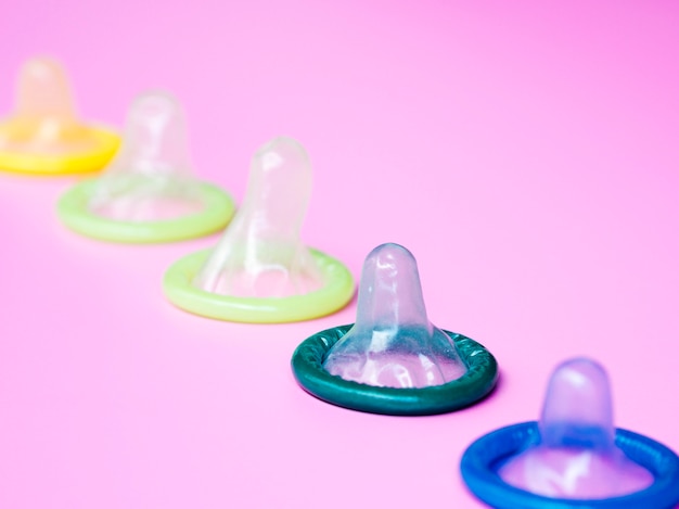 Colourful unwrapped condoms on pink background