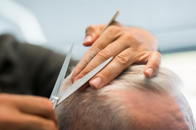 Combing and scissoring grey hair of senior client in barbershop