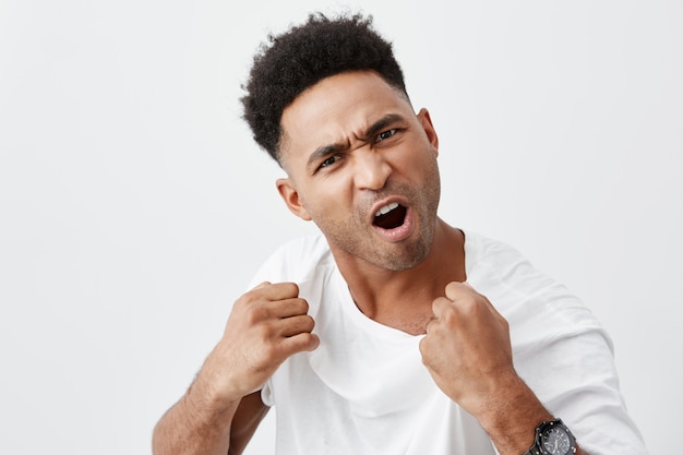 Come here and fight me if you dare. Close up of mature aggressive attractive dark-skinned man with curly hair in white tshirt being ready to fight, angry talking to man who offended him