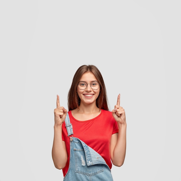 Come upstairs and look. Happy emotive Caucasian woman points upwards with both index fingers