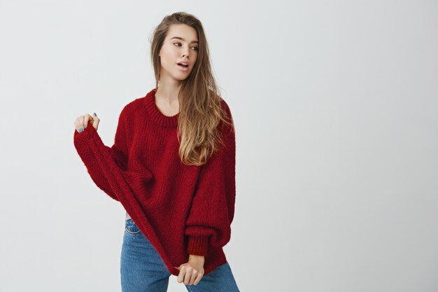 Comfort before fashion. Portrait of feminine gorgeous caucasian woman looking aside with sensual expression and pulling sweater with hands, posing like model for magazine or online-store