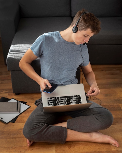 Uomo comodo utilizzando laptop e smartphone a casa in quarantena per lavorare