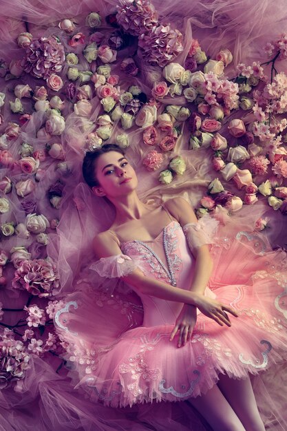 Comfortable. Top view of beautiful young woman in pink ballet tutu surrounded by flowers. Spring mood and tenderness in coral light.