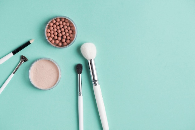 Compact and bronzed pearls with various makeup brushes on green background