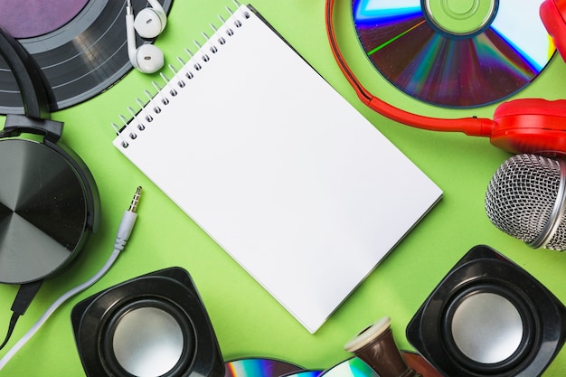 Compact discs; speaker; headphone; earphone around the spiral notepad on green background