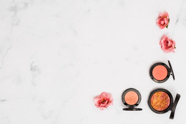Compact face powder with pink rose on marble textured backdrop