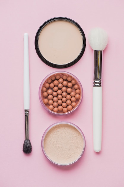 Compact powders; bronzing pearls and makeup brushes on pink surface