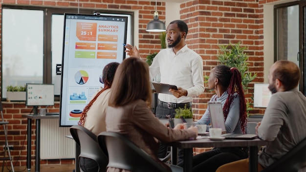 Company employee presenting business strategy with charts on monitor, planning project. Workmates analyzing financial statistics on display, working together on company development.