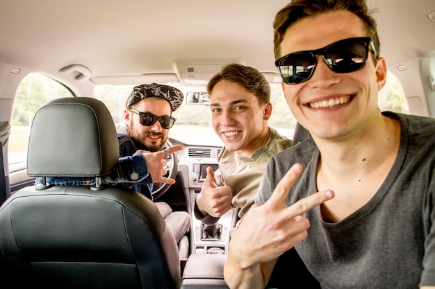 Company of joyful friends sitting in car in journey