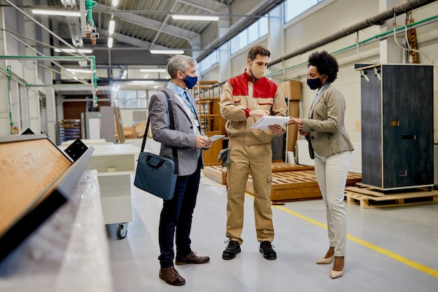 Company managers and leading carpenter analyzing reports at wood factory during coronavirus pandemic