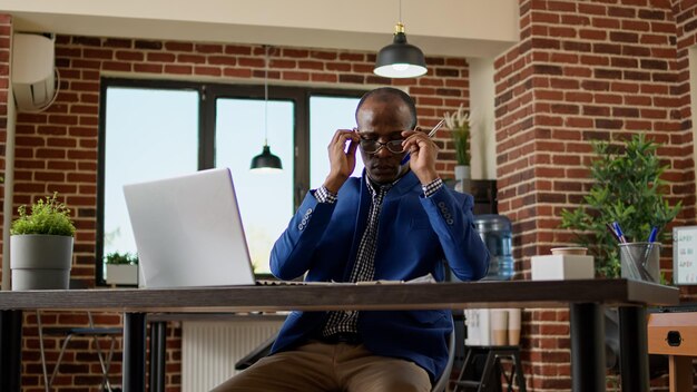 Company worker using documents and research on laptop to take notes. Young office employee working on paperwork report with website information on computer, browsing internet app.