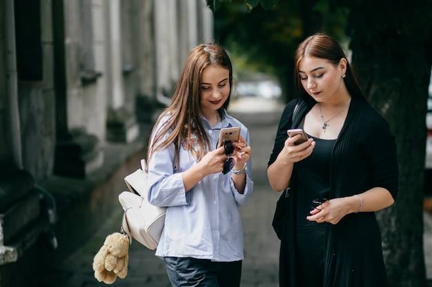 company of young friends with smartphones walking in city