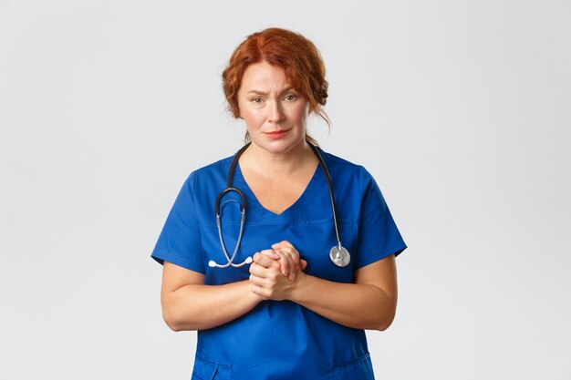 Compassionate and worried female doctor, medical worker clasp hands together and begging people stay home, social distance and wear masks