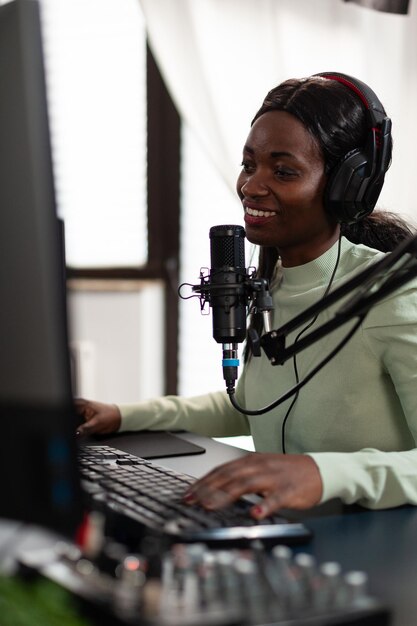 Competitive african american gamer smiling while talking with players on live streaming during online tournament. Pro streamer playing space shooter video games using RGB computer equipment.