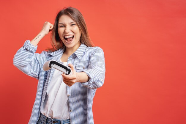 Competitive girl celebrates winning holding game joystick controller on red wall.