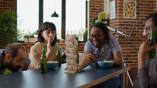 Competitive person enjoying society game play with friends at board games gathering, having fun with wooden square tower and building blocks. Cheerful friends playing toy competition.