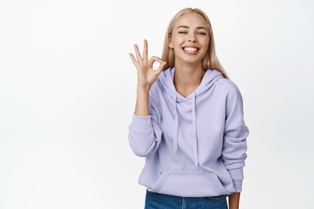 褒め言葉。満足しているように見える笑顔の若い女性、大丈夫、OKジェスチャーを示し、承認にうなずき、白に正のフィードバックを与える