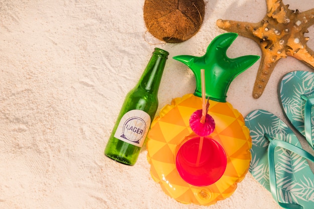 Foto gratuita composizione della noce di cocco delle stelle marine dei sandali del cocktail della bottiglia sulla sabbia