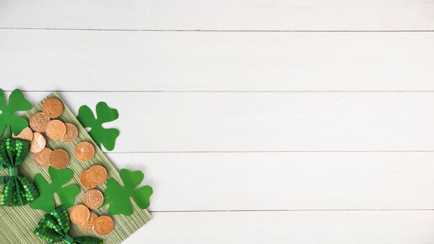 Composition of bow ties near coins and green paper clovers on board