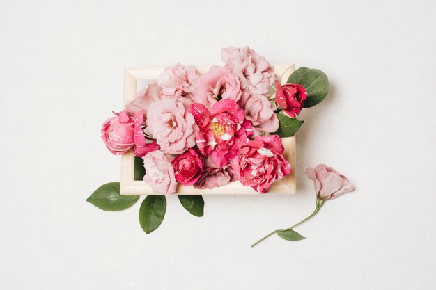 Composition of fresh beautiful pink flowers in box near leaves