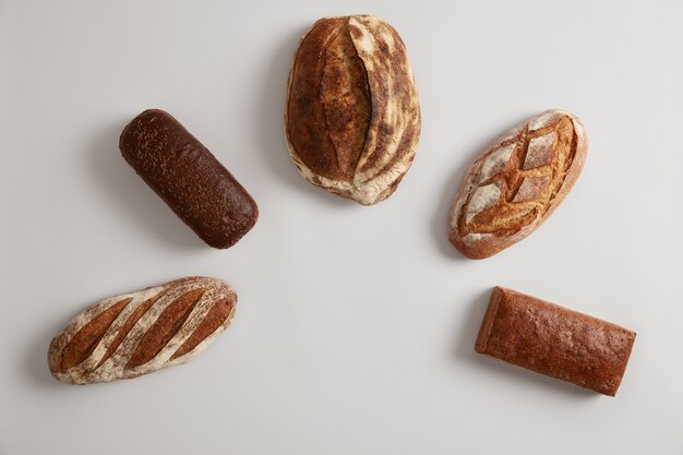 Composition of fresh organic bread of different types arranged in half circle against white background. Wholegrain buckwheat multigrain rye bread baked at bakery. Rustic natural bio product.