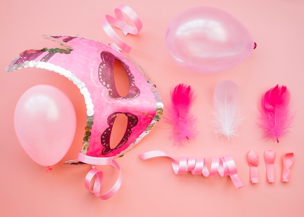 Composition of mask near balloons and feathers 