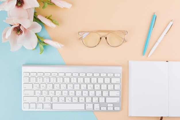 Composition of notepad, keyboard, eyeglasses, flowers and pens