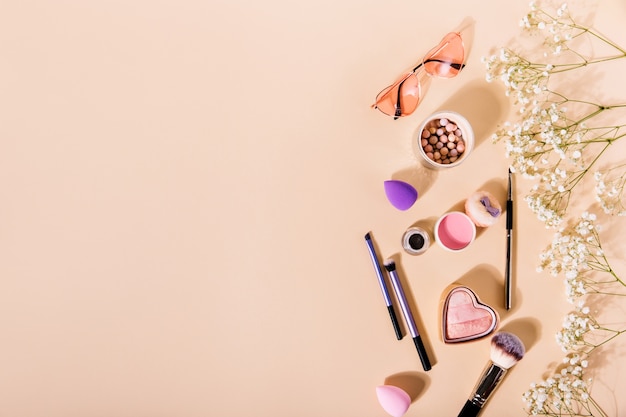 Free photo composition of pink blush, makeup brushes and glasses in shape of hearts lies among cute flowers