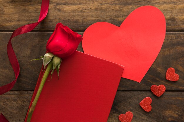 Composition of red flower near ribbon, hearts and paper