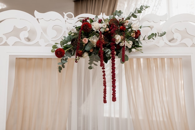 Composition on the white wedding arch made of eucalyptus and bordeaux flowers