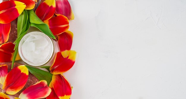 チューリップの花びらに囲まれた白の瓶にココナッツオイルを入れた組成物、コピースペースのある上面図