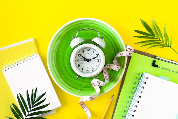 Composition with plate, alarm clock and measuring tape on a colored background. Diet concept and weight loss plan, copy space.