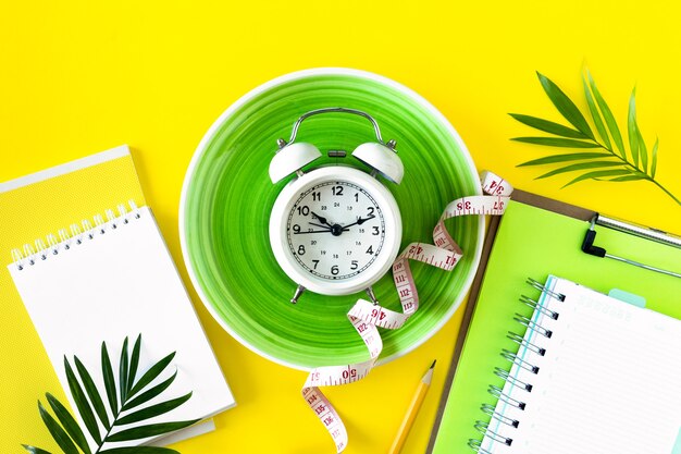 Composition with plate, alarm clock and measuring tape on a colored background. Diet concept and weight loss plan, copy space.