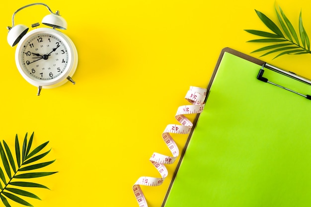 Composition with plate, alarm clock and measuring tape on a colored background. Diet concept and weight loss plan, copy space.