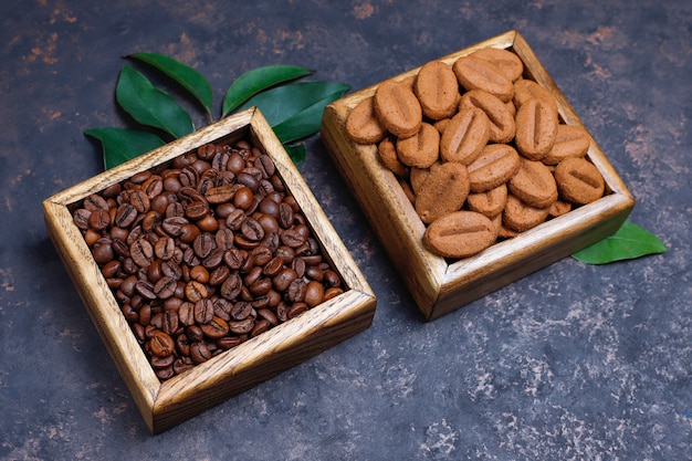 Composition with roasted coffee beans and coffee bean shaped cookies on dark brown surface