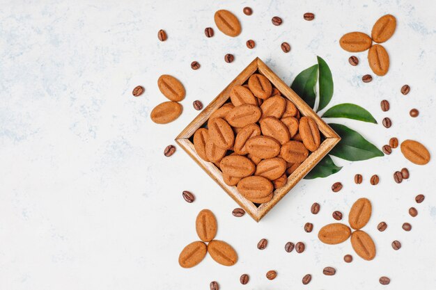 Composition with roasted coffee beans and coffee bean shaped cookies on light surface