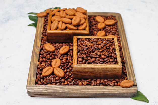 Composition with roasted coffee beans and coffee bean shaped cookies on light surface